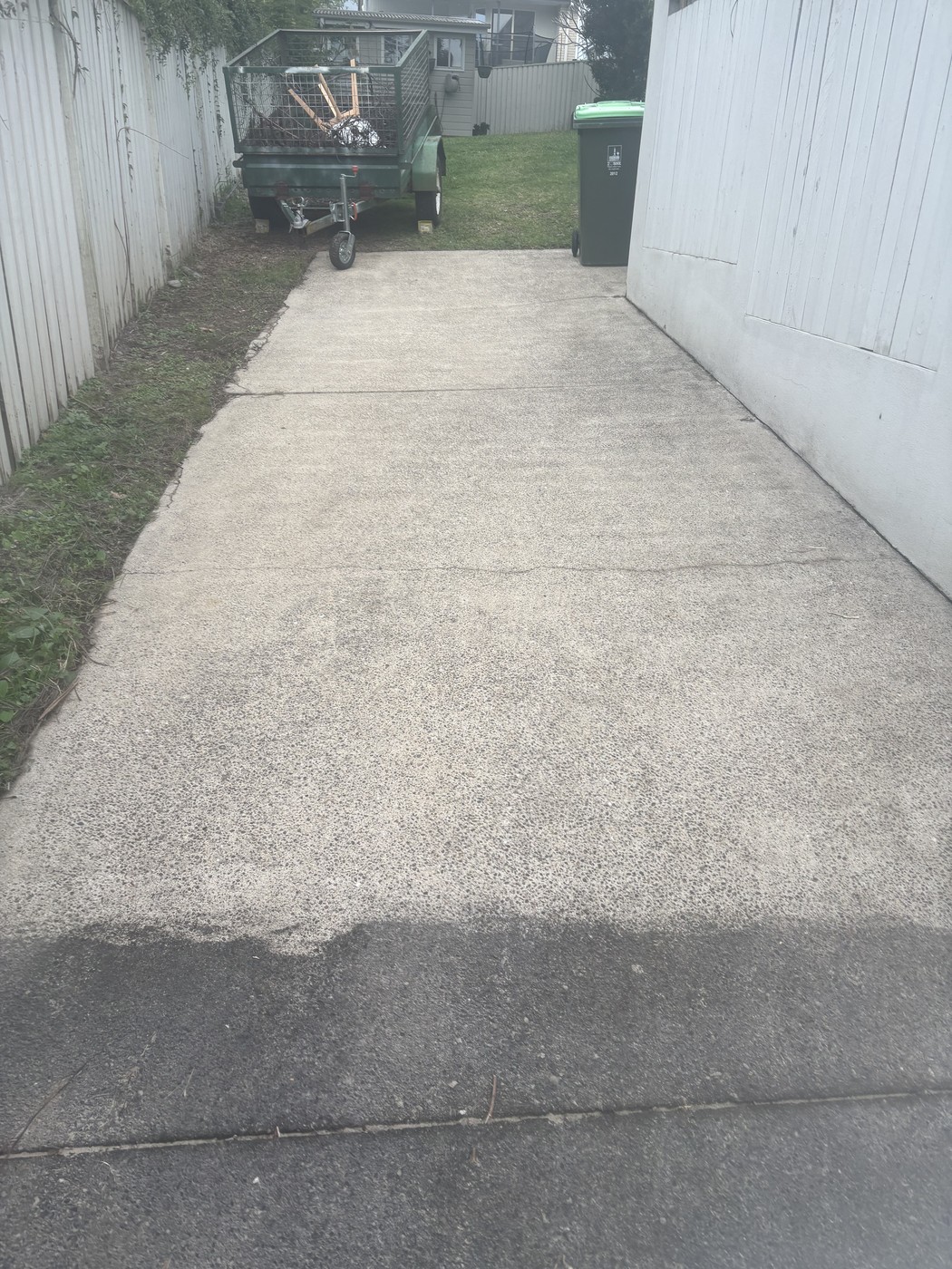 Concrete side driveway cleaned back to bare grey, running past a garden-waste trailer and bin.